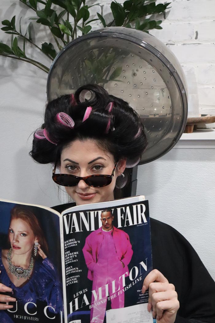 A woman with curlers in her hair reading Vanity Fair